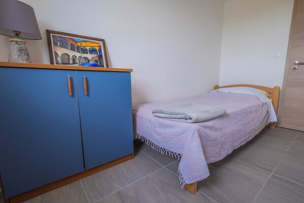 A bedroom with a bed, a blue wardrobe, a lamp, and a painting on the wall.