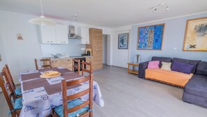 Un salon moderne avec un canapé gris, une table à manger avec des chaises et un coin cuisine doté de meubles blancs et d’un meuble en bois.