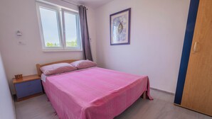 Une chambre à coucher comprenant un lit, une table de chevet, une fenêtre avec des rideaux, un tableau encadré accroché au mur et une armoire en bois.