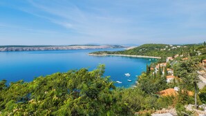 Une ville côtière bordée d’une mer d’un bleu éclatant, entourée de verdure et de bâtiments aux toits rouges.