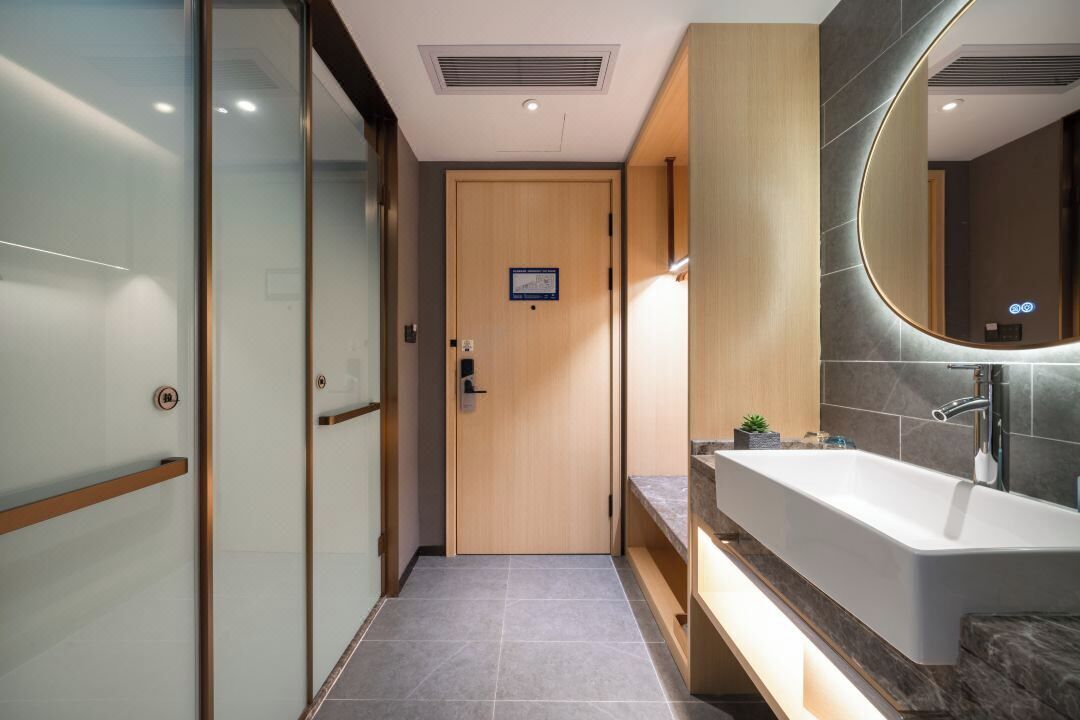 A modern bathroom with a large sink, a mirror, and a wooden door.