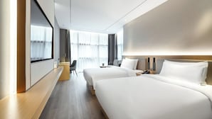 Ein modernes Hotelzimmer mit zwei Betten, einem Schreibtisch und einem großen Fenster mit Vorhängen.