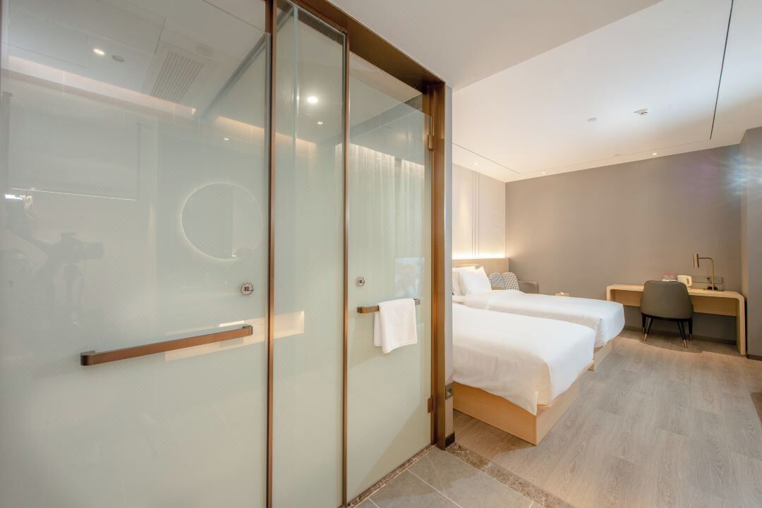 Et moderne hotelværelse med glasvæg, to senge, et skrivebord og en stol.