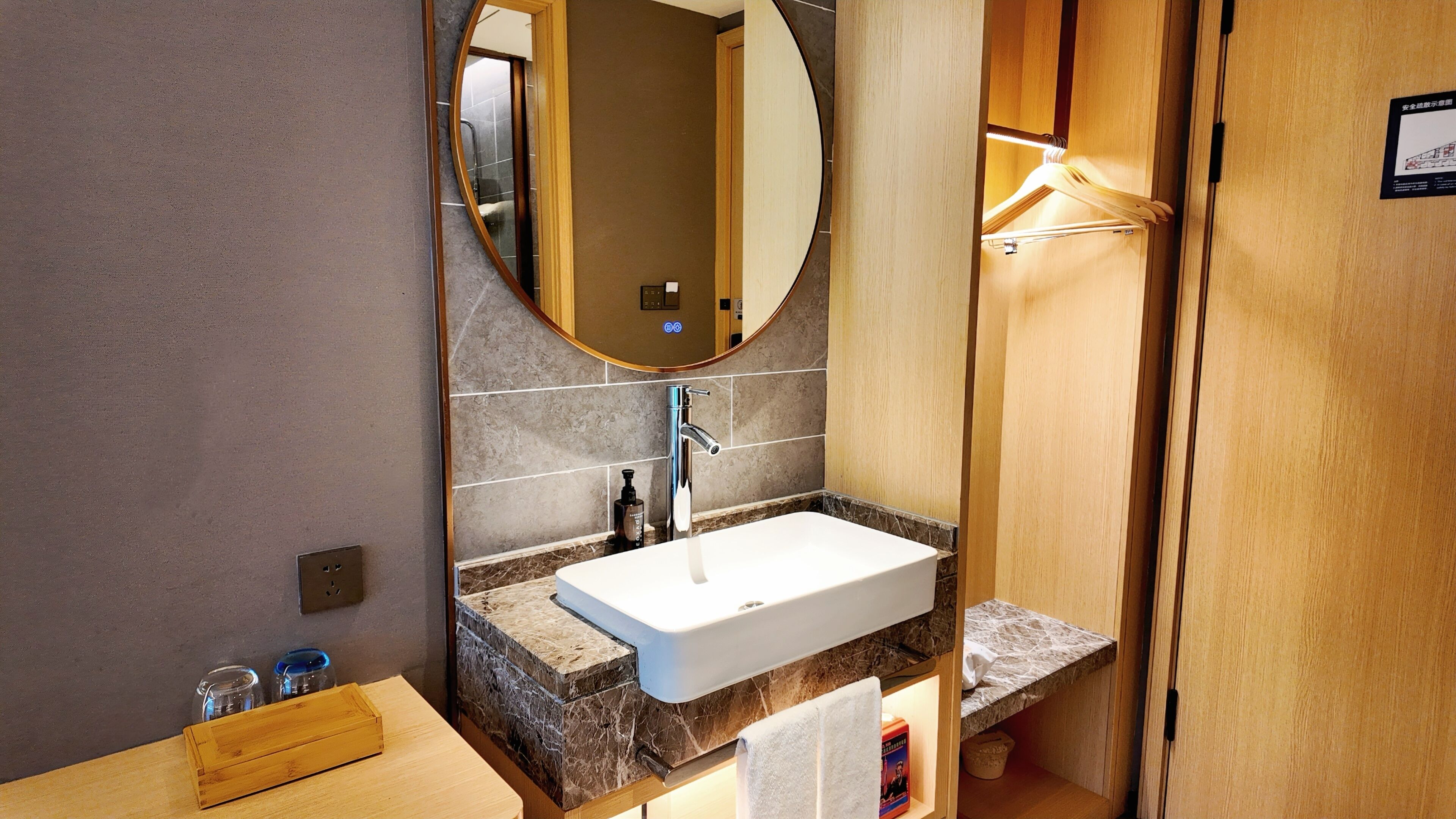 A modern bathroom with a marble countertop, a white sink, a mirror, and a wooden door.