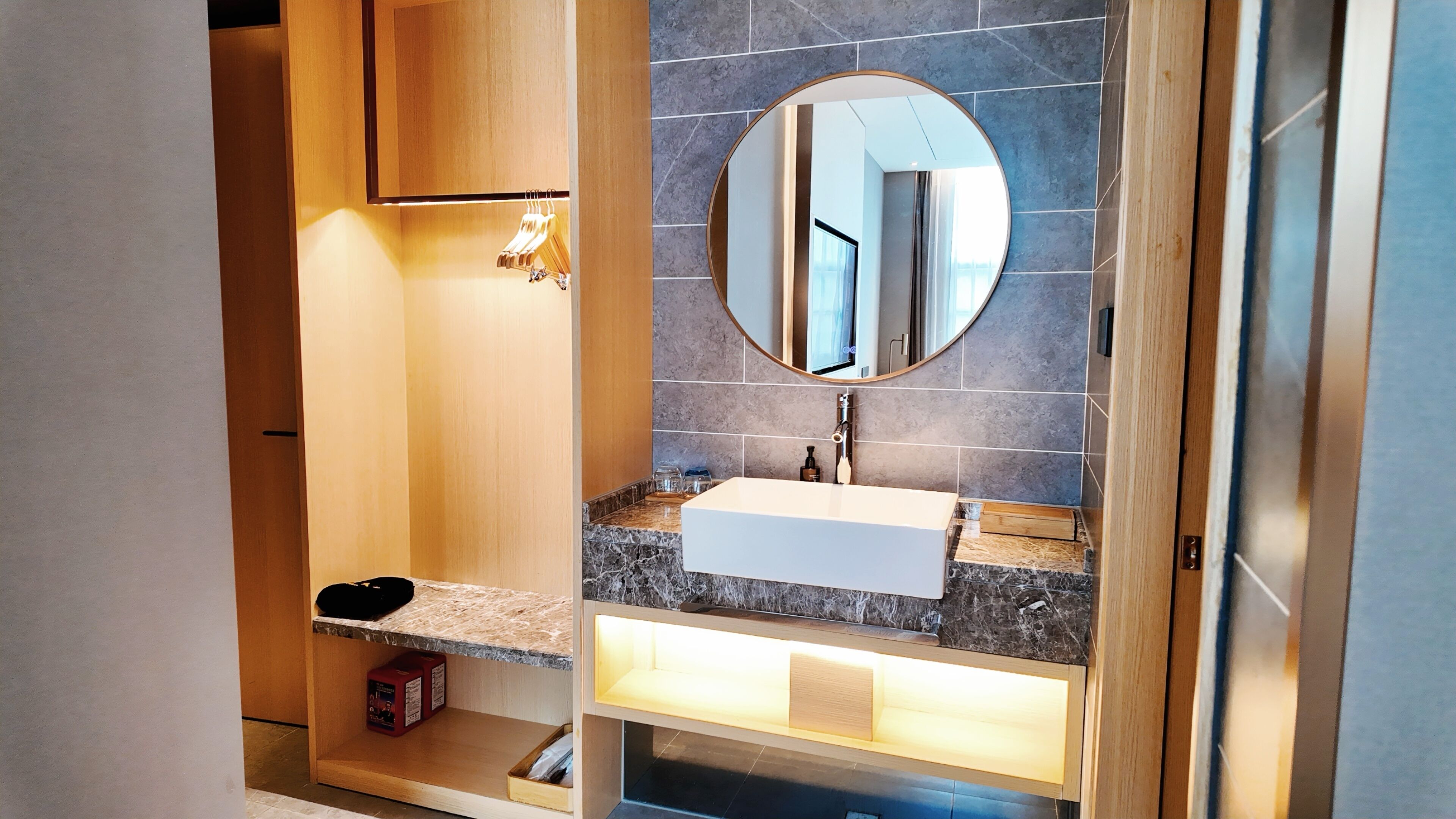 A modern bathroom with a marble countertop, a white sink, and a round mirror.
