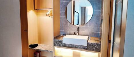 A modern bathroom with a marble countertop, a white sink, and a round mirror.