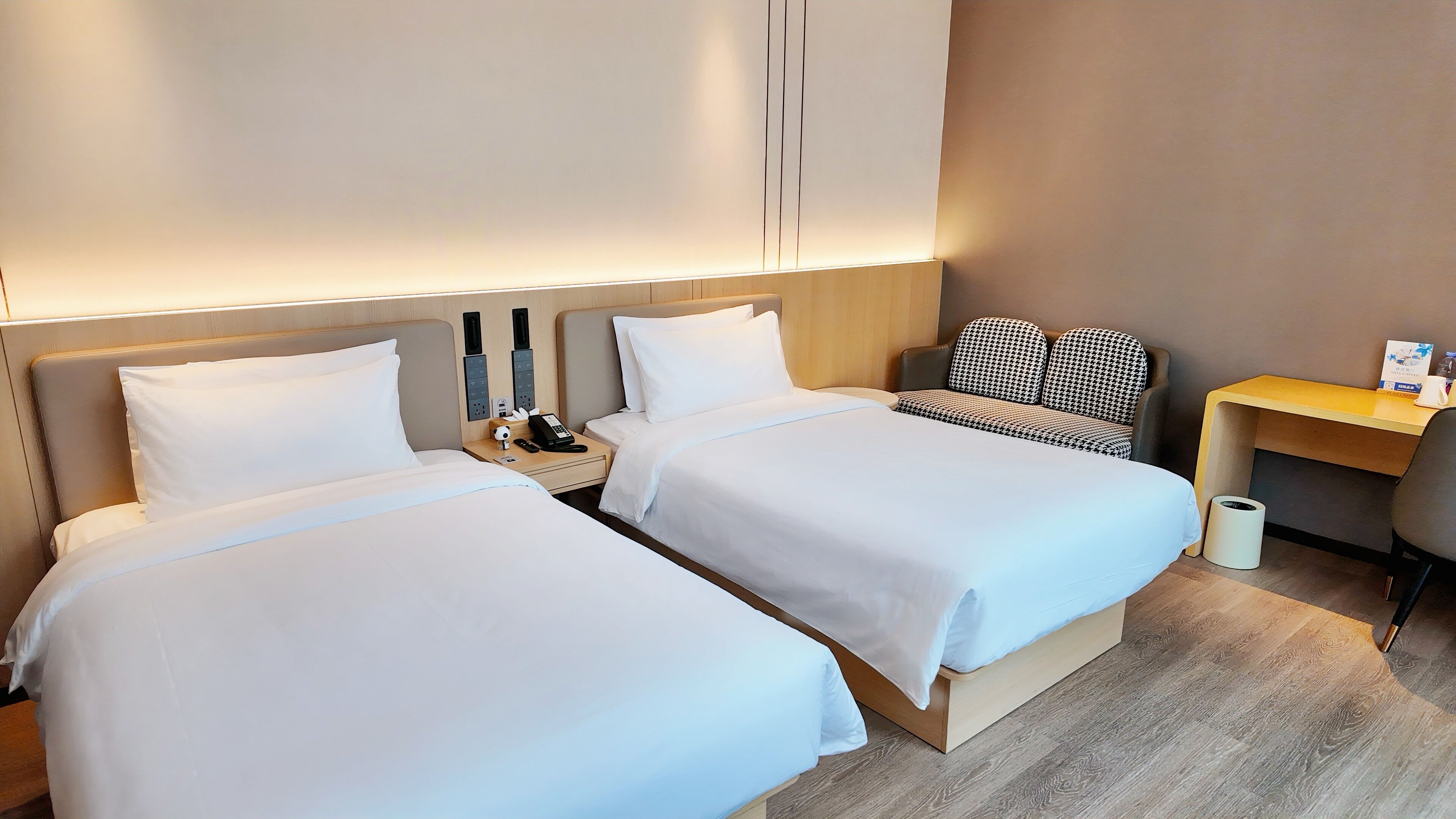 Habitación de hotel con dos camas, un escritorio y un bote de basura.