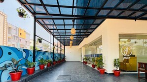 Un espacio al aire libre techado con plantas en macetas, una escalera y la entrada a un edificio con puerta de vidrio.