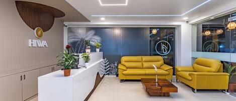 Un área de recepción moderna con un mostrador blanco, sofás amarillos y una mesa de centro de madera.