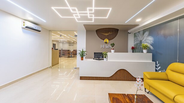Un área de recepción moderna con un mostrador blanco, un sofá amarillo y una mesa de centro de madera.