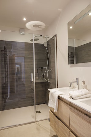 Bathroom features a glass-enclosed shower, vanity with sink and mirror, and a wooden cabinet.