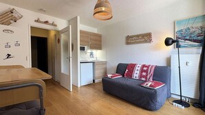 En kompakt opholdsstue med tekøkken, spiseplads og sofa med mønstret tæppe.