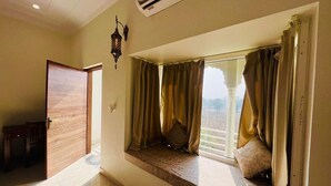 A room with a large window, a wooden door, and a small table. - Roop Garh Palace (Jamwa Ramgarh)