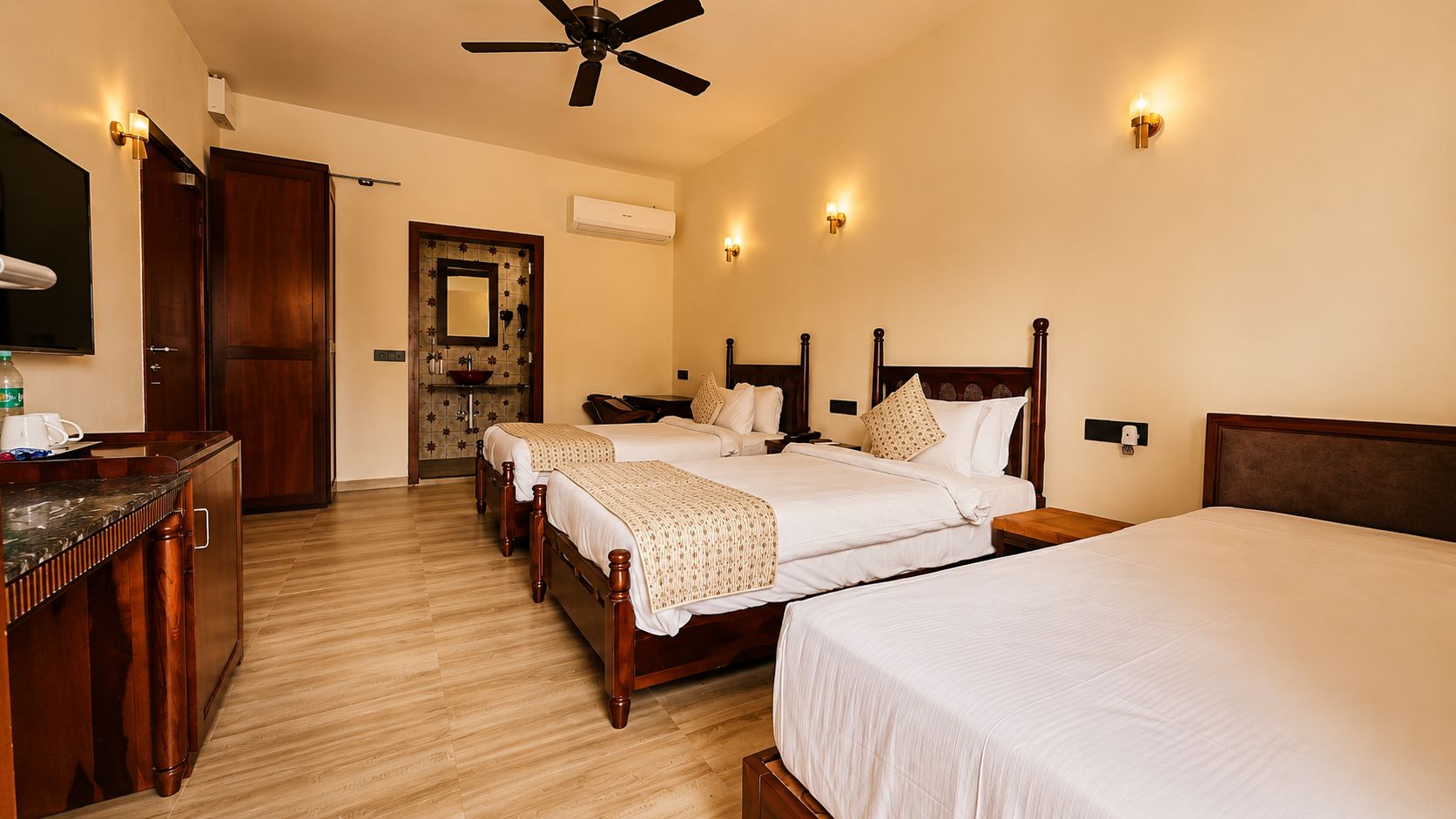 Habitación de hotel con cuatro camas individuales, un aparador de madera, un ventilador de techo y aire acondicionado instalado en la pared.