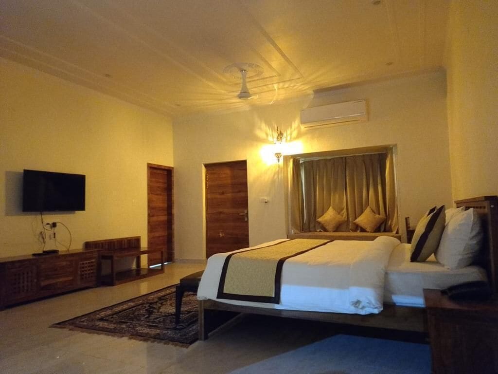 A hotel room with a bed, a TV, a wooden bench, and a ceiling fan.