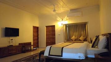 A hotel room with a bed, a TV, a wooden bench, and a ceiling fan.