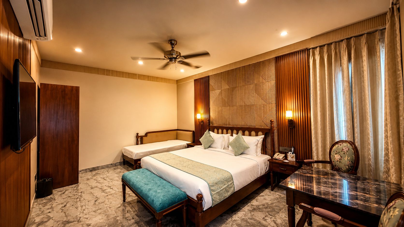 A hotel room with a bed, a desk, a chair, a television, and a ceiling fan.