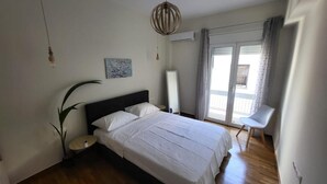 A bedroom with a bed, a bedside table, a potted plant, a hanging light fixture, and a view of the outside through a window with curtains. - 2 bd Renovated Flat at Acropolis (Athens)