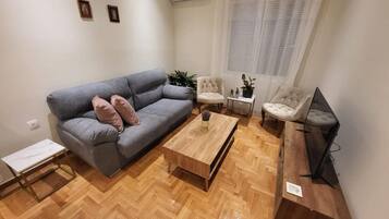 Ein modernes Wohnzimmer mit einem grauen Sofa, zwei Sesseln, einem Couchtisch und einem Fernsehschrank.