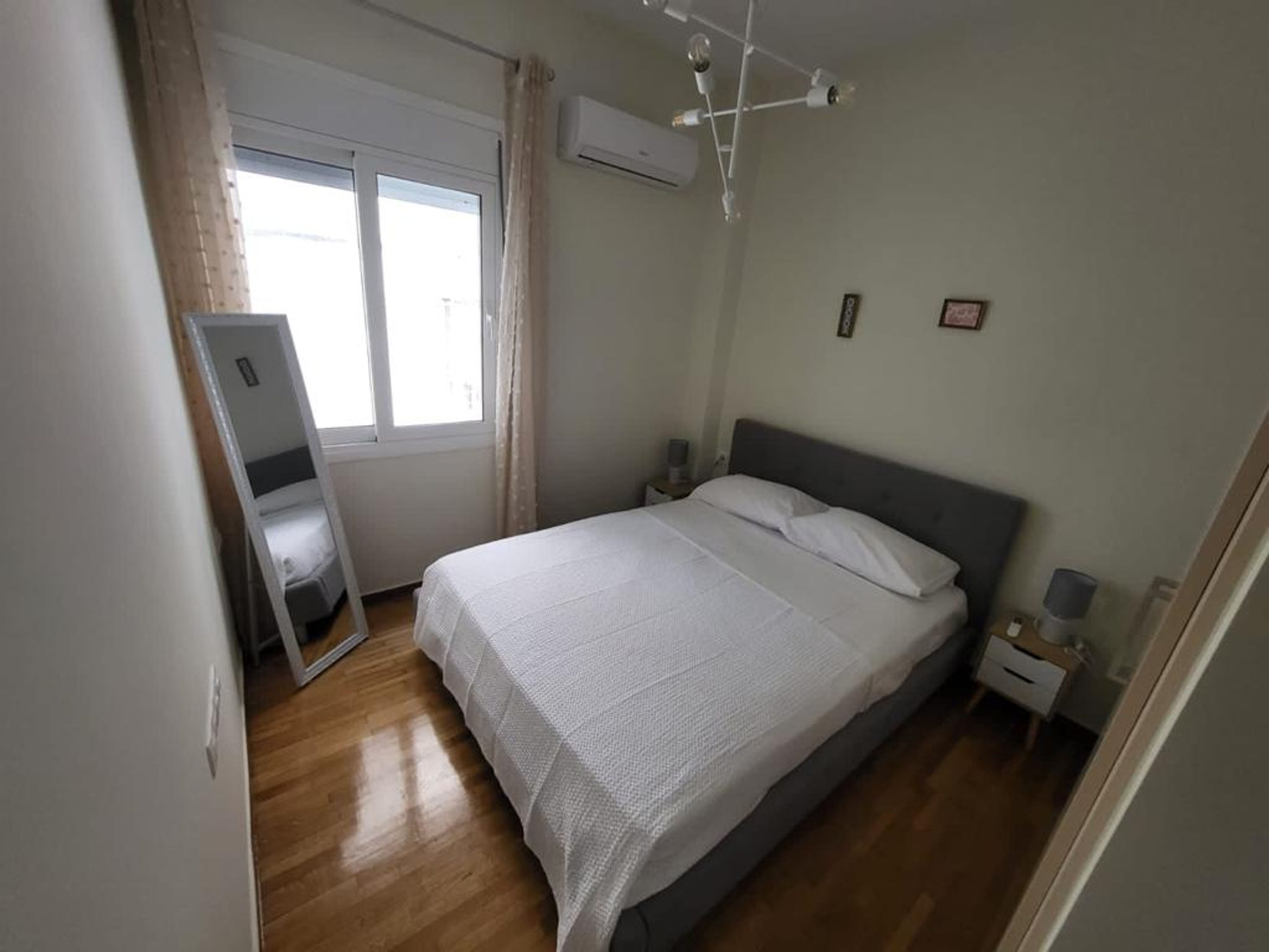 A bedroom with a bed, a window, an air conditioning unit, and a bedside table.