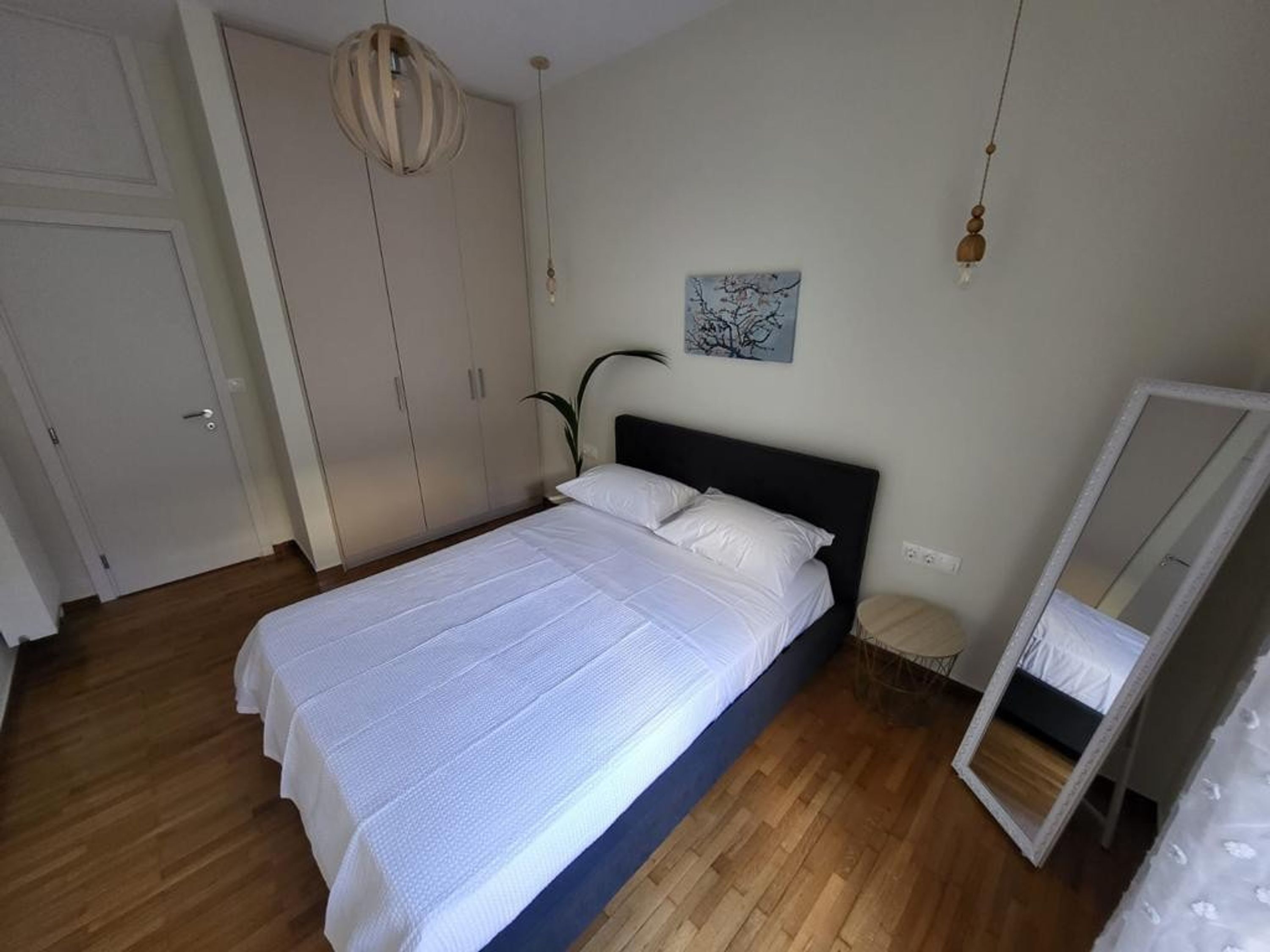 A bedroom with a bed, a wardrobe, a mirror, and a hanging light fixture.