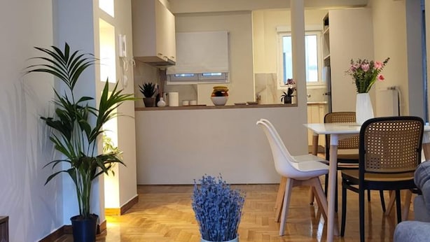 A modern kitchen with white cabinets, a dining area with a white table and chairs, and a living room with a grey sofa and a coffee table. - 2 bd Renovated Flat at Acropolis (Athens)