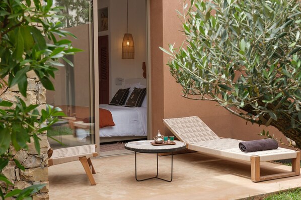 A sunlit outdoor seating area with a lounge chair, a small round table, and a potted plant. - TY HABIBI (Marrakech)