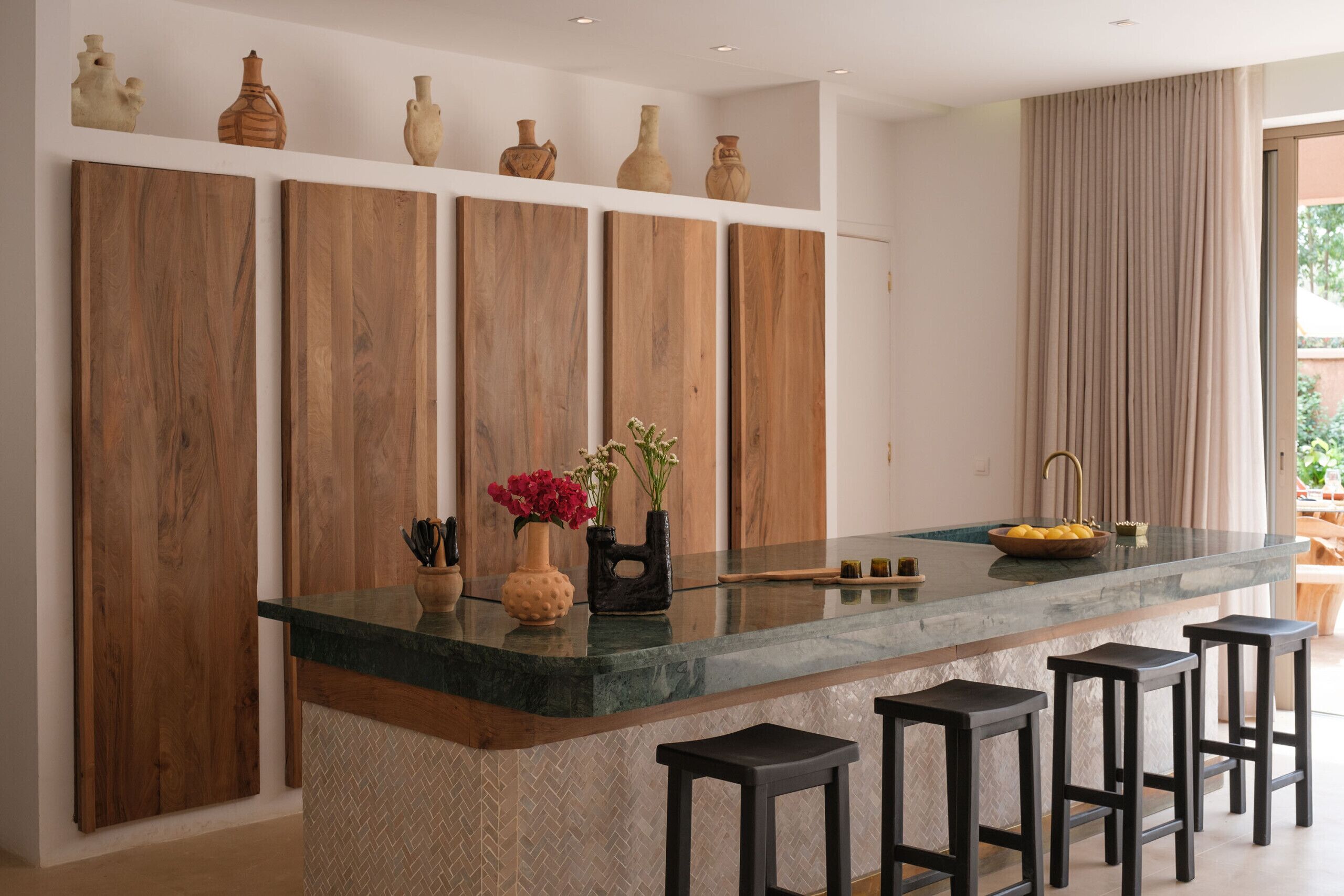 A kitchen with a marble island, wooden cabinets, and a large window with curtains.