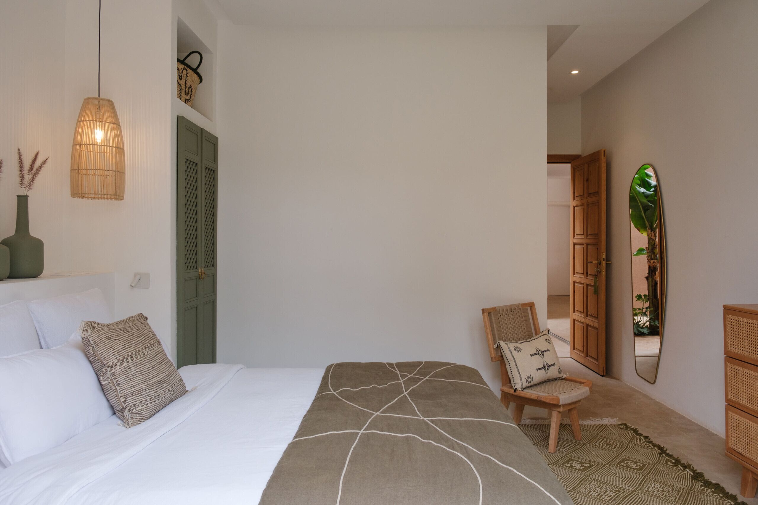 Een slaapkamer met een bed, een stoel, een spiegel en een hanglamp.
