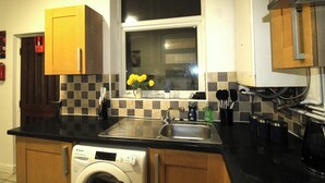 Une cuisine de taille réduite, équipée d’un lave-linge, d’un évier et de meubles de rangement en bois.