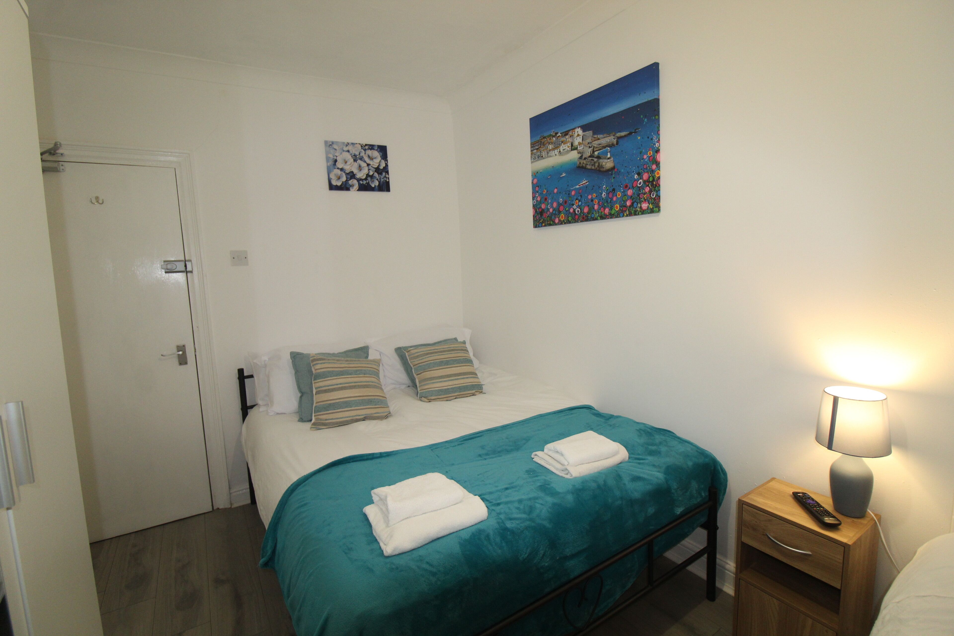 A bedroom with a bed, a nightstand with a lamp, and two paintings on the wall.