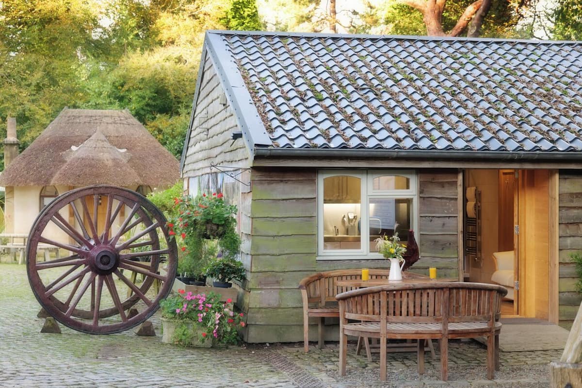 Eine rustikale Blockhütte mit einem Reetdach, einer hölzernen Bank und einem großen Wagenrad davor.