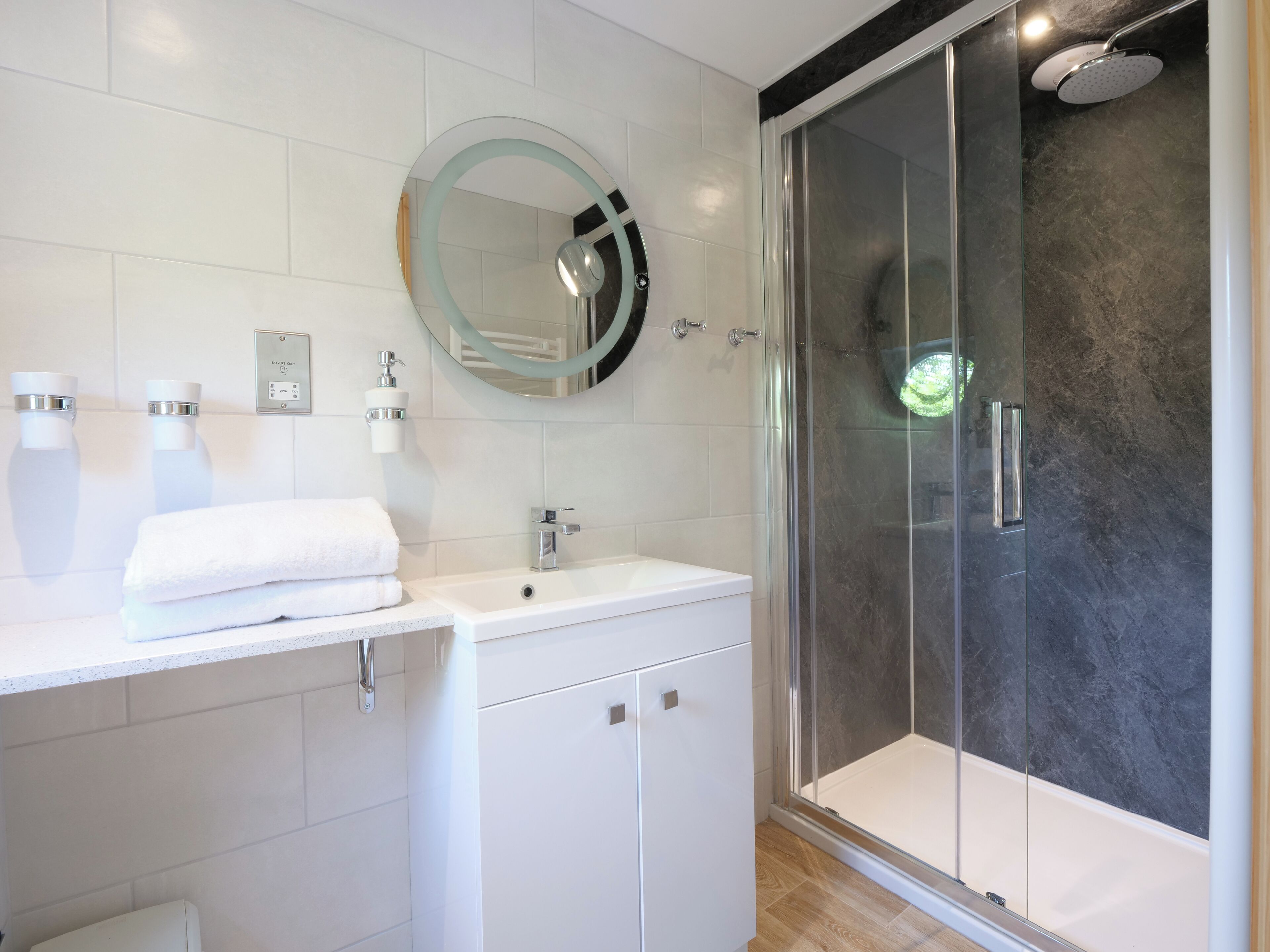 A modern bathroom with a white vanity, a glass-enclosed shower, and a round mirror.
