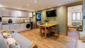 A compact living space with a kitchenette, a dining area, a sofa, and a TV mounted on the wall.