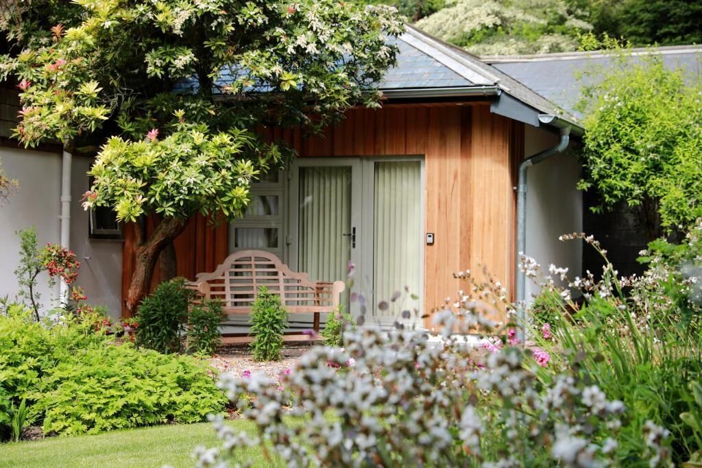 A small wooden house with a front porch, a bench, and a garden with various plants and flowers.