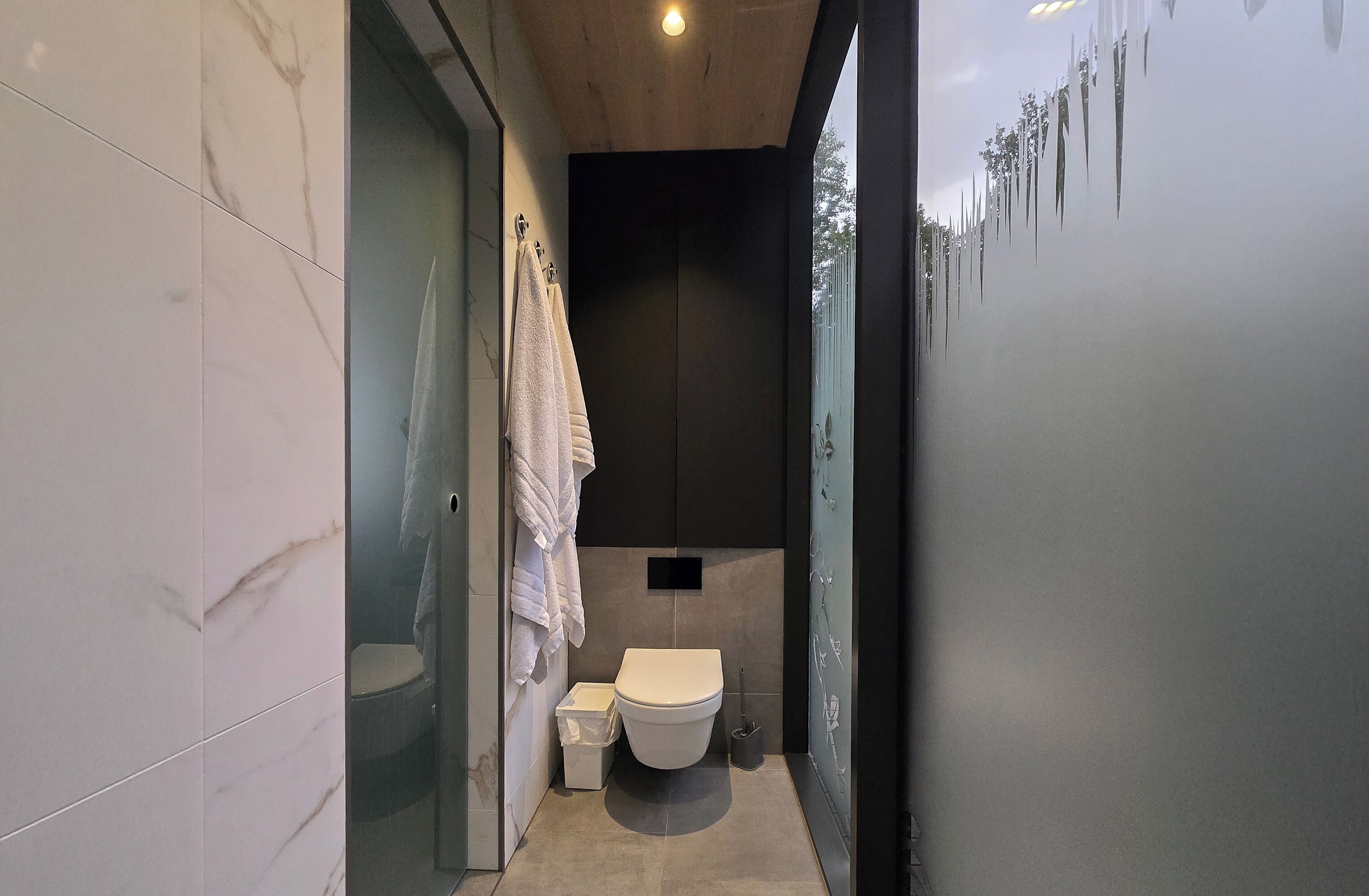 Een moderne badkamer met een toilet, een kleine prullenbak en een handdoek aan een rek.