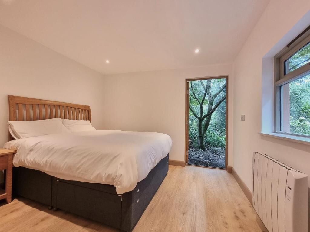 A bedroom with a bed, a nightstand, a window, and a view of trees.