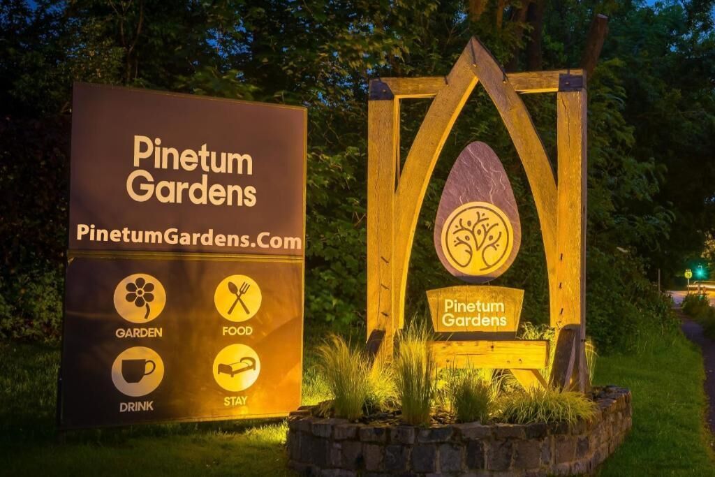 A sign for Pinetum Gardens with icons for garden, food, drink, and stay.
