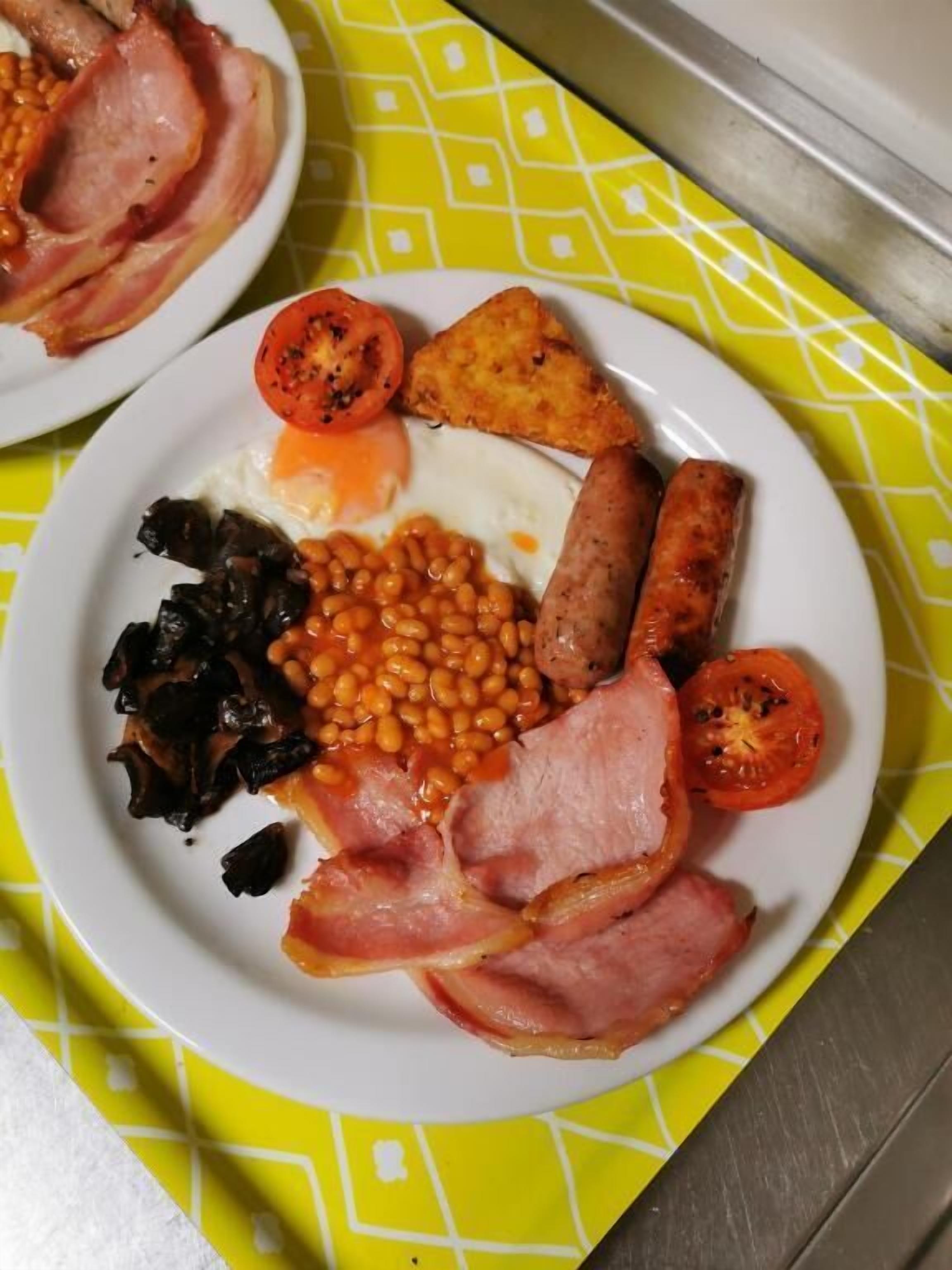 Un piatto di cibo per la colazione con uova, salsicce, fagioli, pomodori e prosciutto.