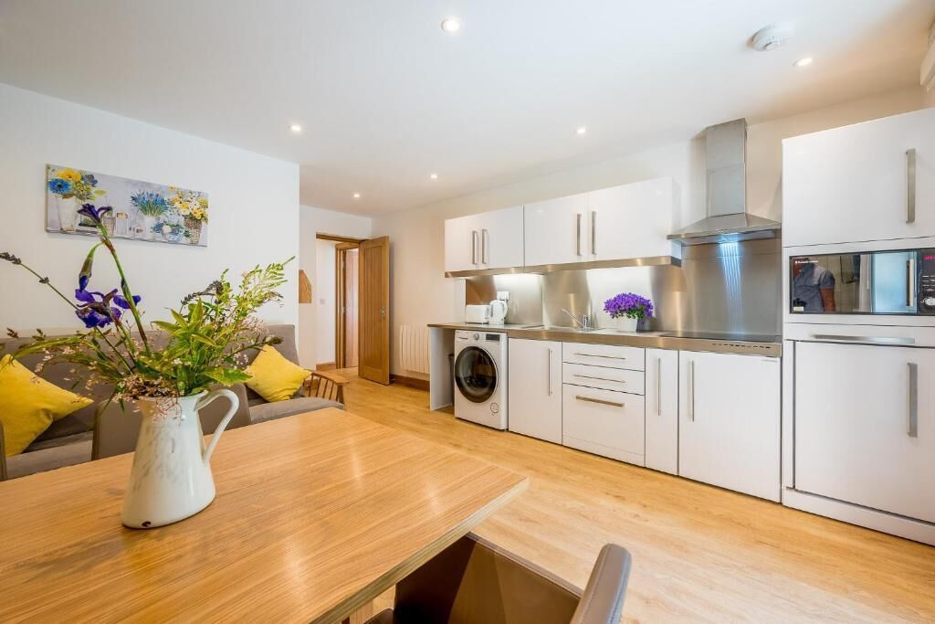 A modern kitchen with white cabinets, a stainless steel range hood, and a built-in oven.