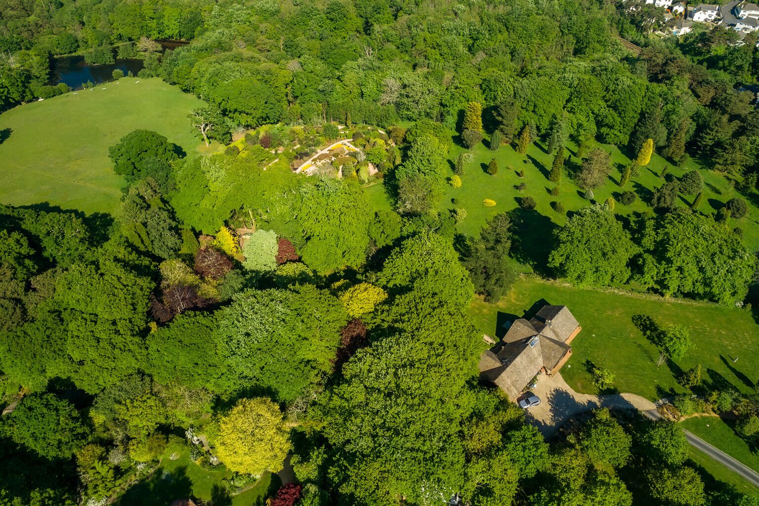 An aerial view of a property with a large green field, a pond, and a house with a sloped roof.