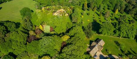 An aerial view of a property with a large green field, a pond, and a house with a sloped roof.