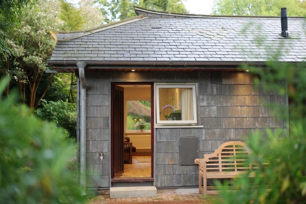 A small, rustic cabin with a dark shingled roof, a wooden door, and a bench outside.