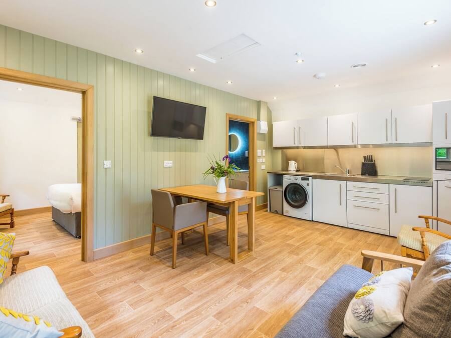 Un espacio habitable compacto con comedor, sofá, lavadora y televisor montado en la pared.