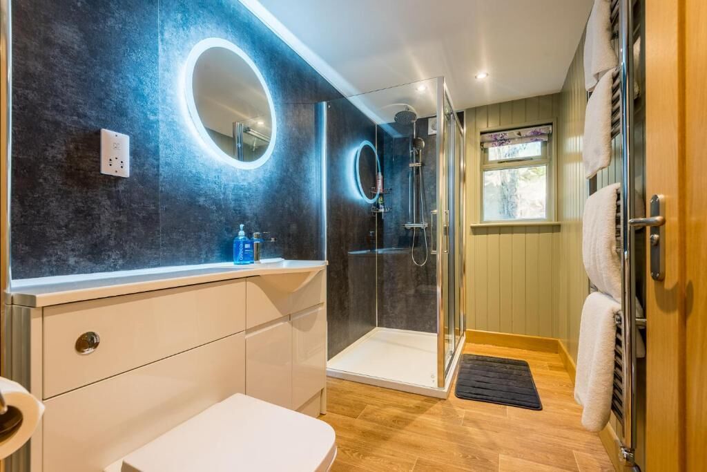 A modern bathroom with a glass shower enclosure, a white sink, and a round mirror.