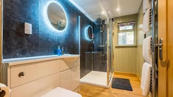A modern bathroom with a glass shower enclosure, a white sink, and a round mirror.
