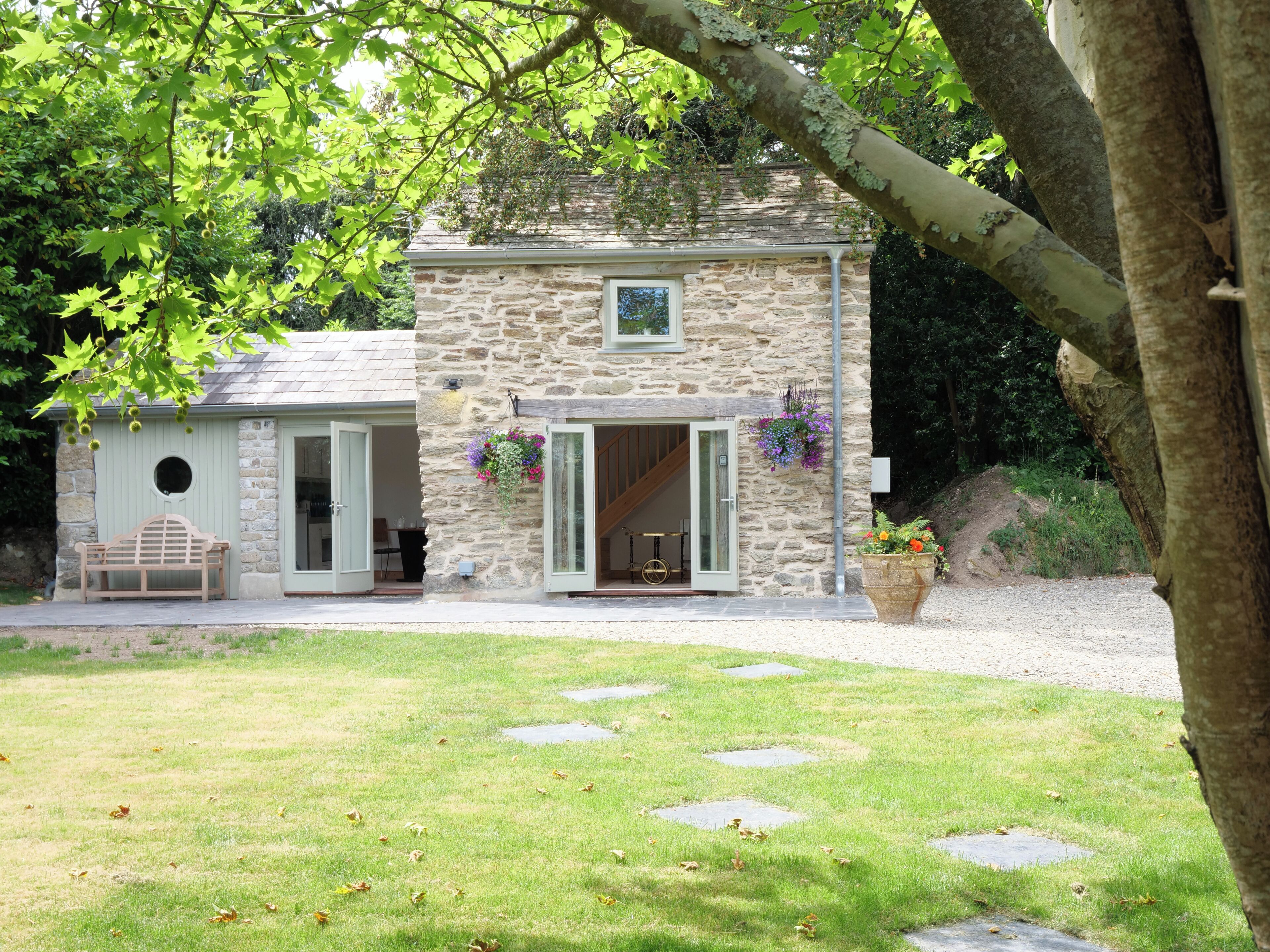A stone building with a small porch and a bench, surrounded by a grassy lawn with stepping stones.