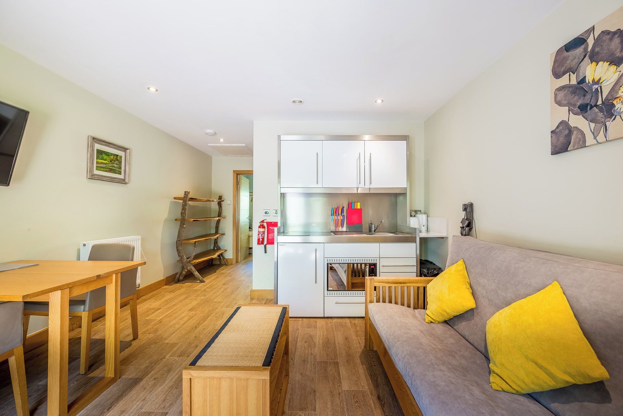 A modern apartment with a dining area, kitchenette, and a living room with a sofa and cushions.