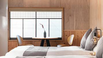 A bedroom with a large window, a round table, two chairs, a bed, and a bedside lamp.