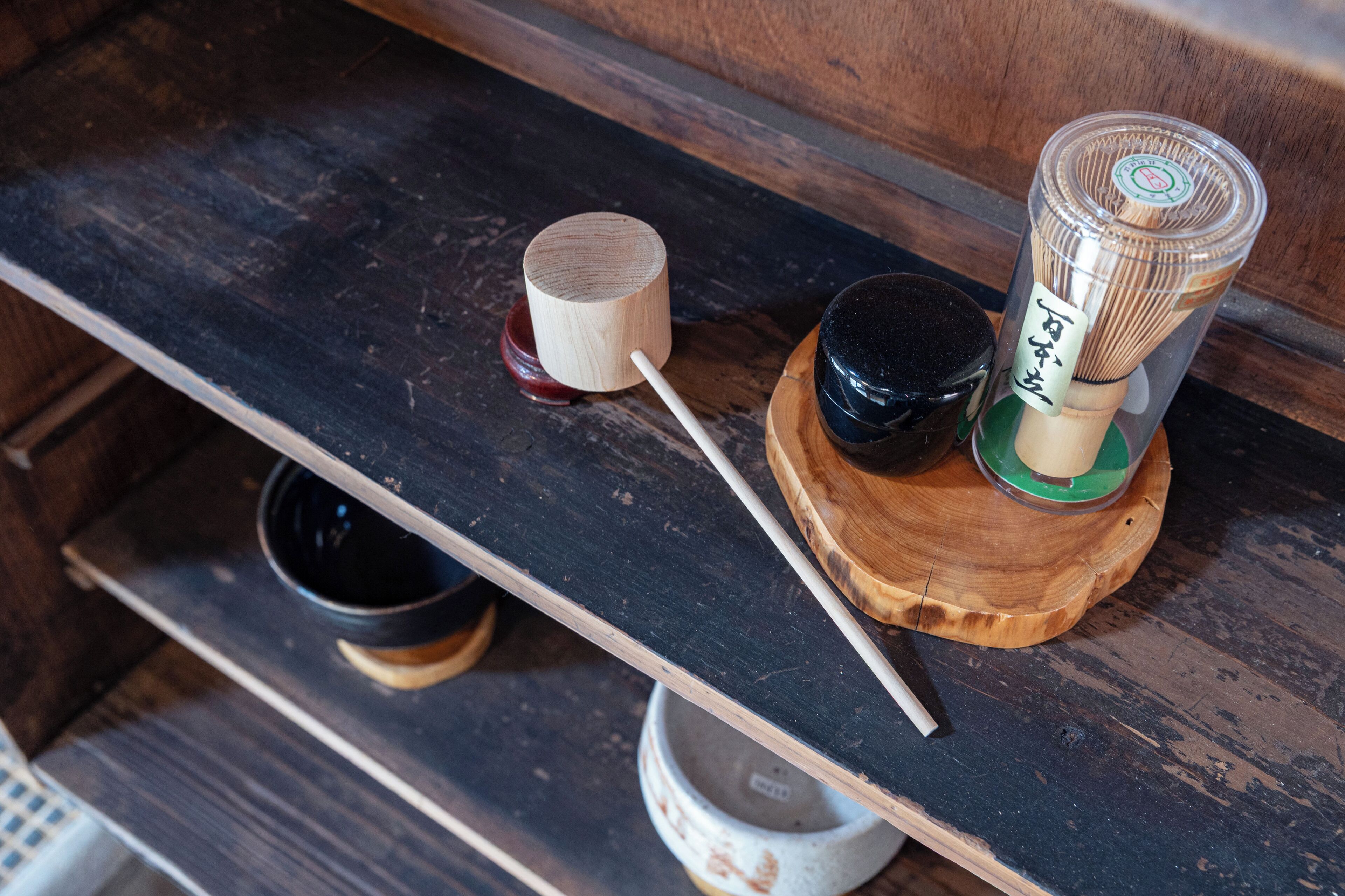 A wooden shelf with a small wooden cup, a black container, and a bamboo brush set.